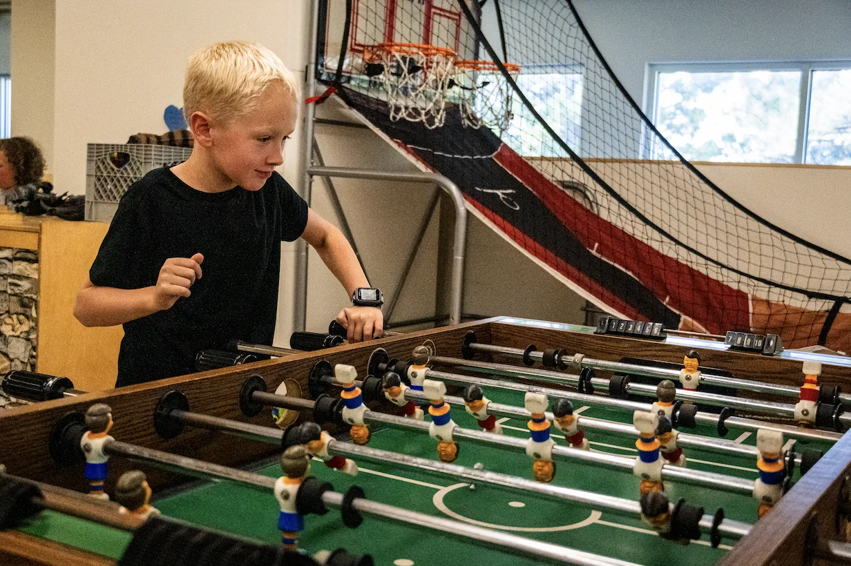 A boy playing foosball next to an arcade basketball hoop at The Hang Out