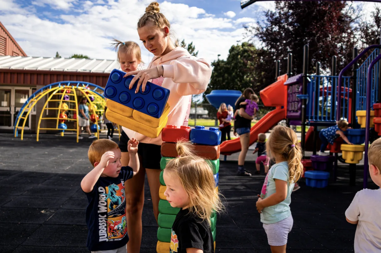 A teacher and toddler stacking oversized building blocks together in the Kids Korner Tumblers classroom