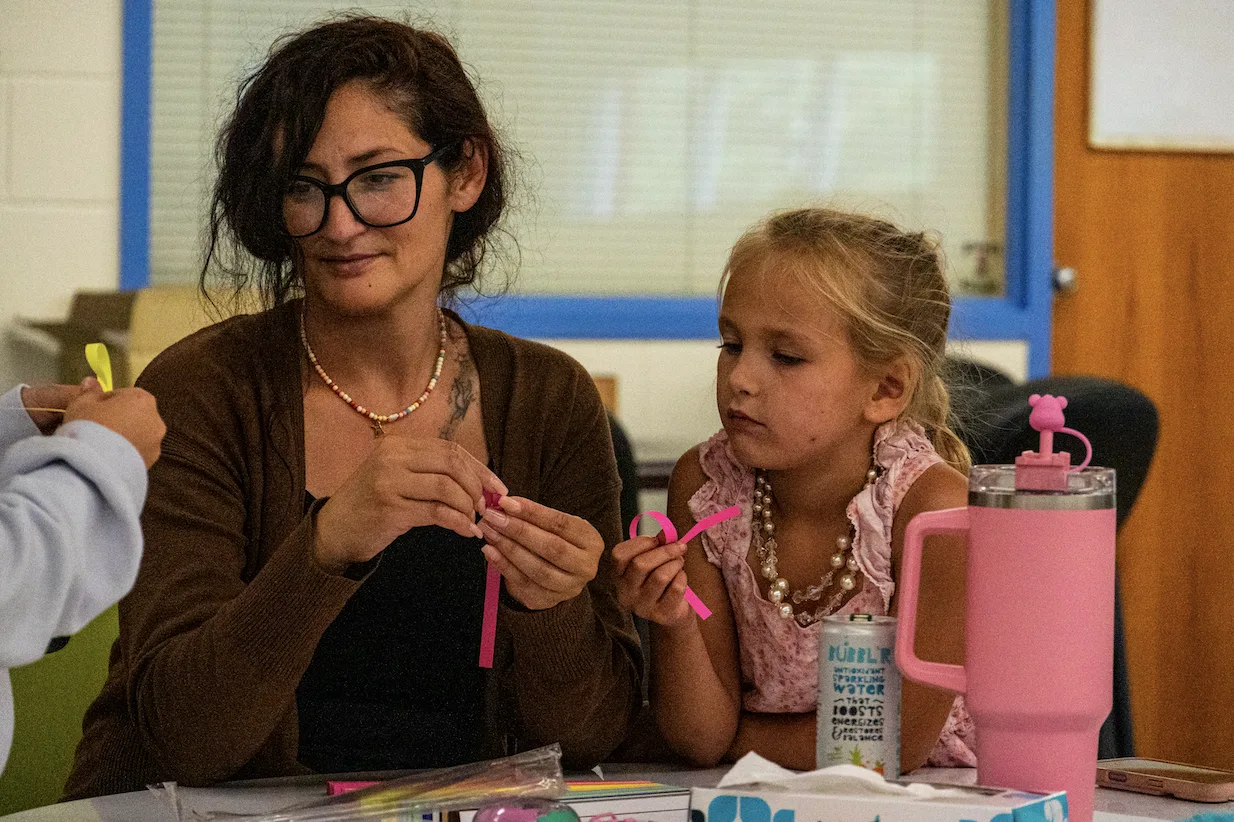 A woman and a young girl calmly focused on making paper crafts together at a table