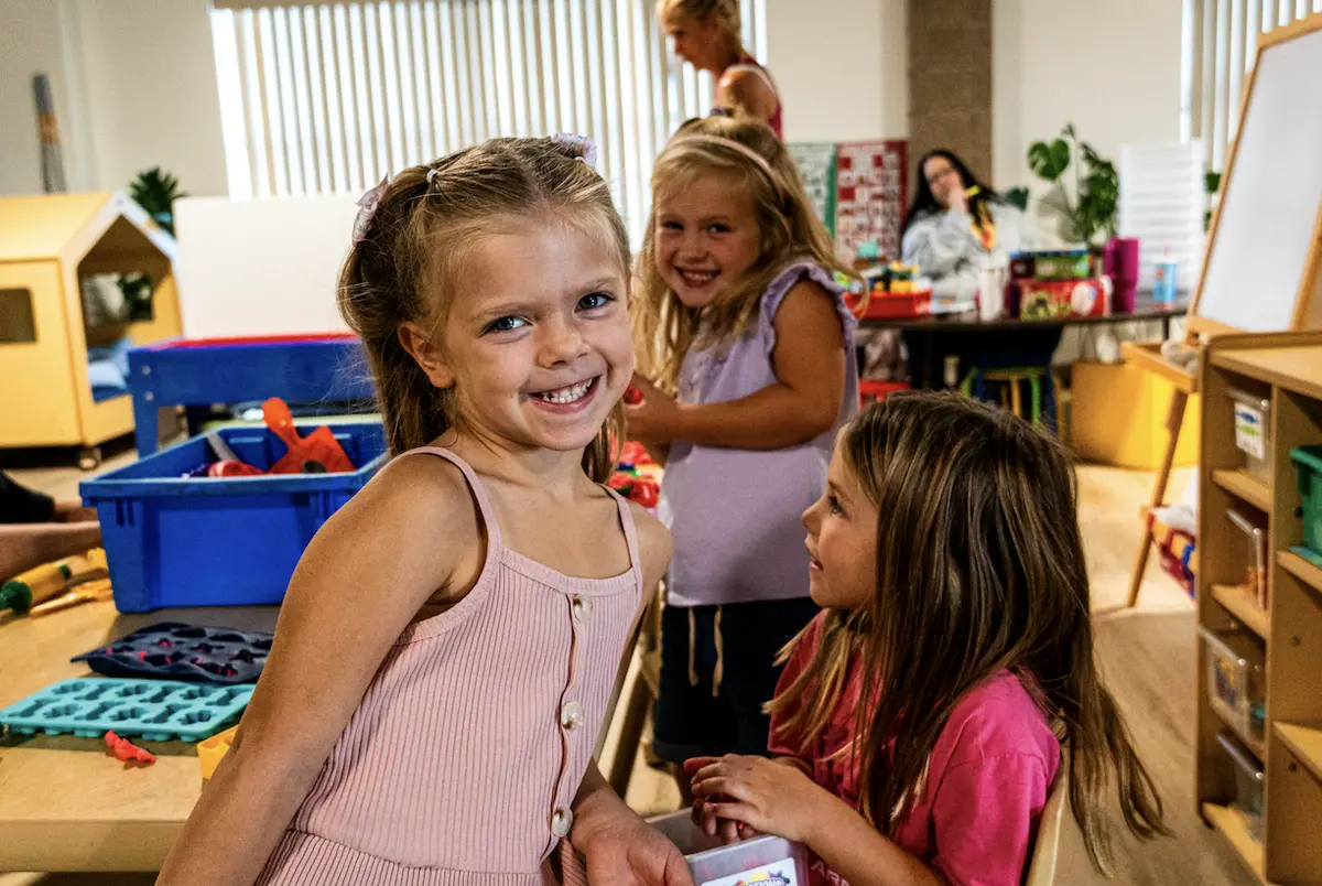 Three preschool friends smiling together at a play table in the Learning Korner classroom