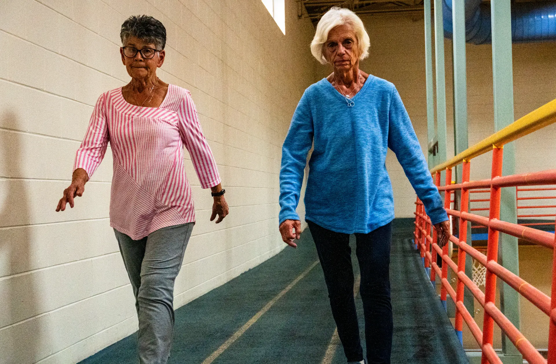 Two members walking together on the elevated indoor walking track above the gymnasium at The Center