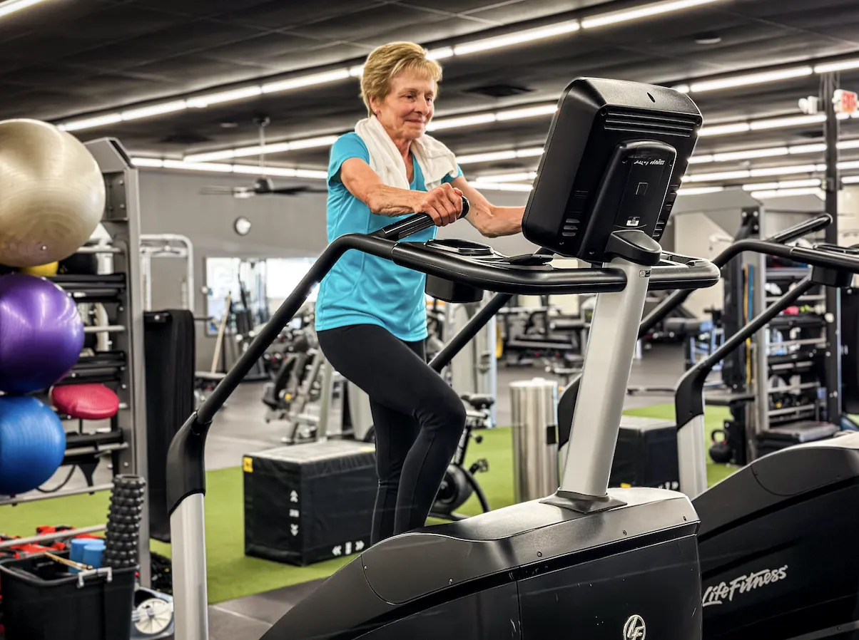 Senior woman smiling while exercising on a Life Fitness stair climber machine at The Training Room