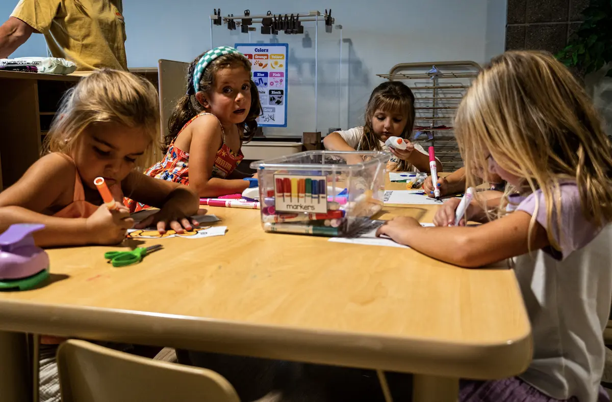 Preschoolers coloring worksheets with markers around a classroom table