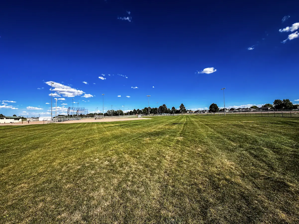 Baseball and softball field with dirt infield, backstop and light poles under a clear sky at The Center