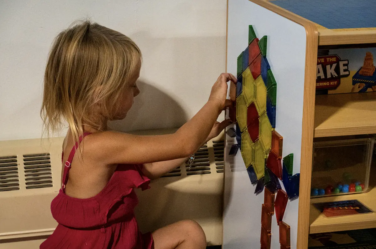 A preschooler building a pattern with magnetic tiles on her own