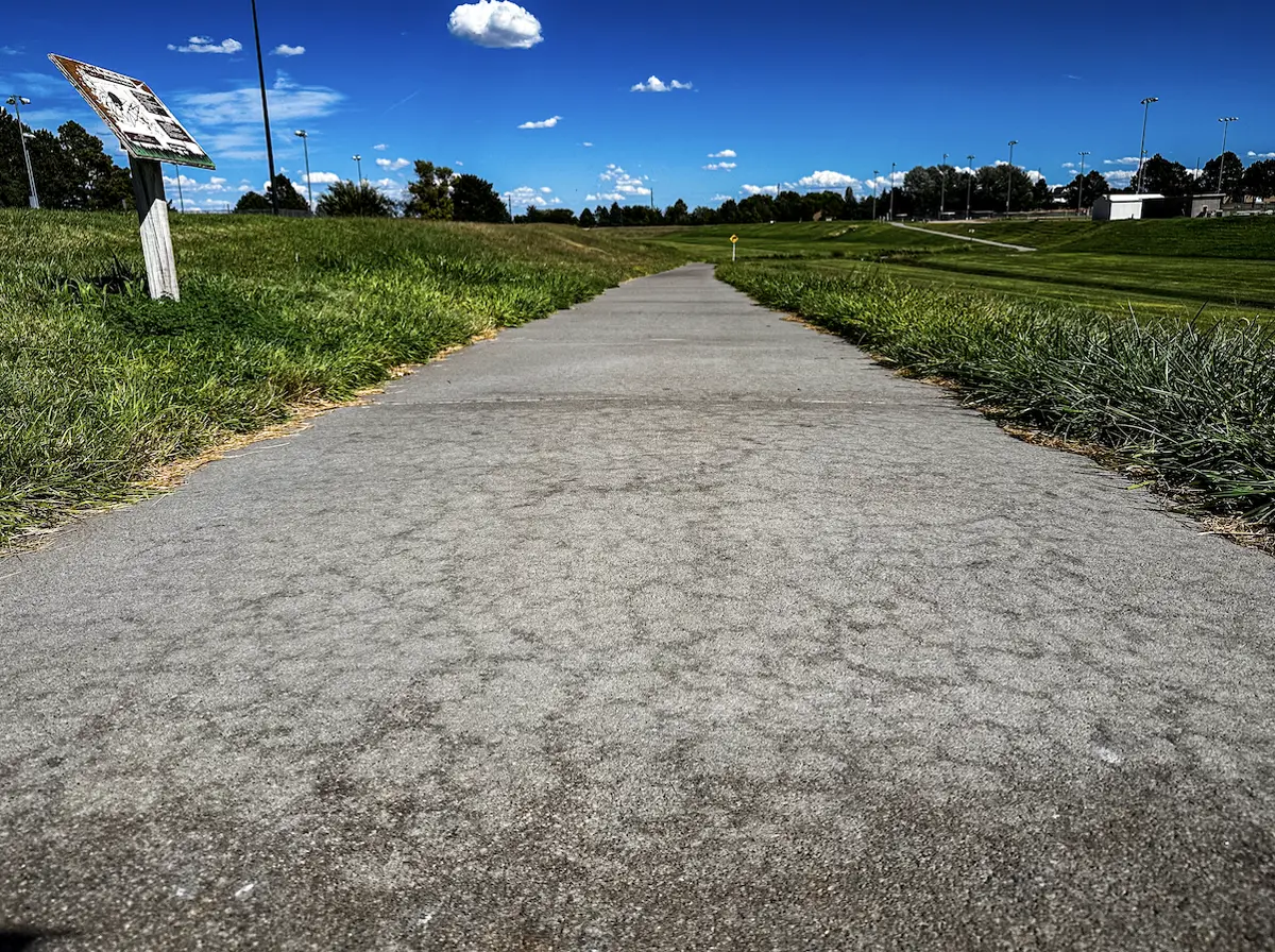 Paved outdoor walking and running trail winding through green grass and open sky at The Center
