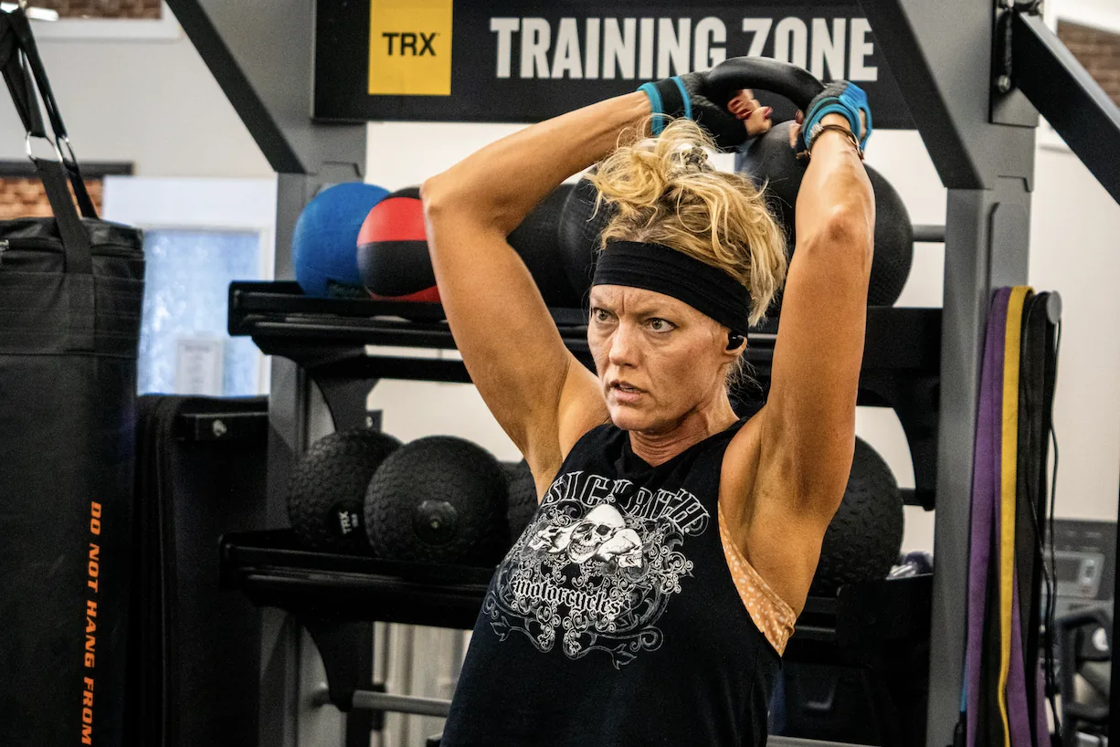 Member pressing a kettlebell overhead in the TRX functional training zone at The Training Room