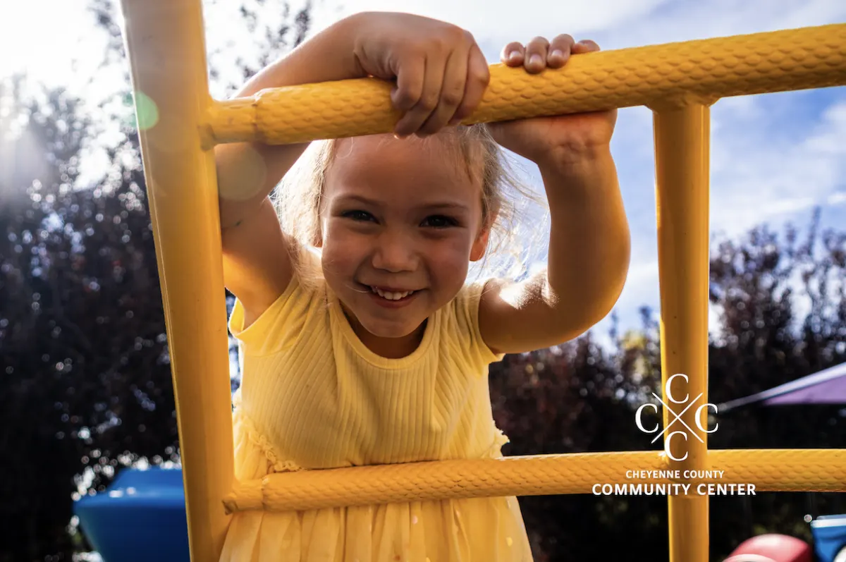 A smiling young girl on yellow monkey bars at a sunny playground