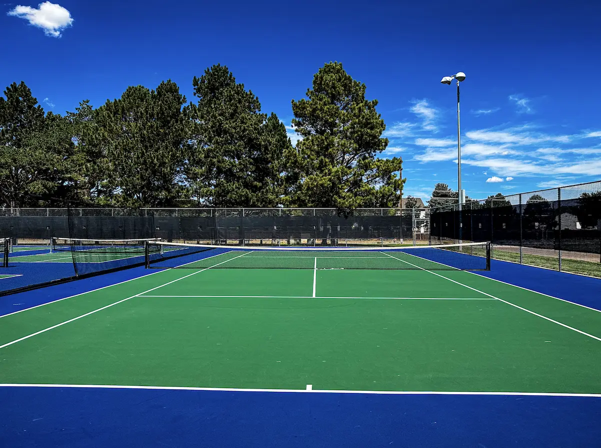 Outdoor tennis court with green and blue playing surface, net and fenced perimeter at The Center