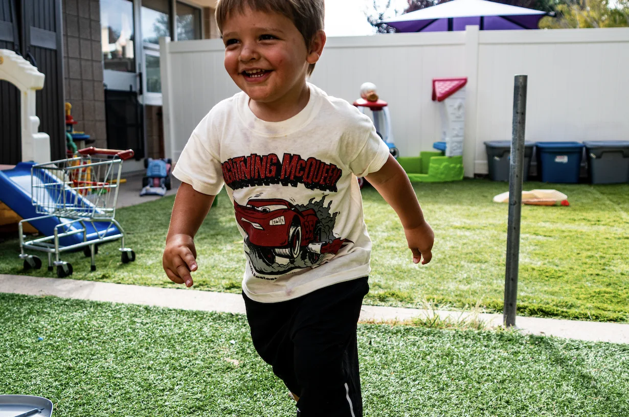 A toddler running joyfully across the outdoor play area at Kids Korner