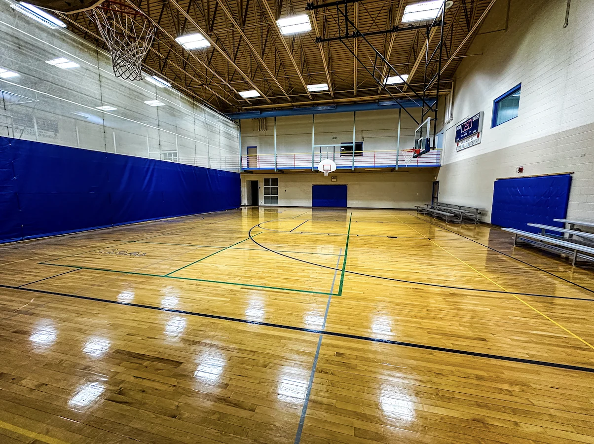 Court-level view of The Center's gym with basketball hoops, hardwood flooring and blue divider padding