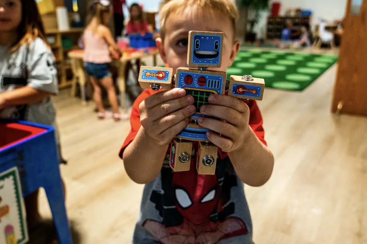 A preschooler proudly holding up a wooden robot he built