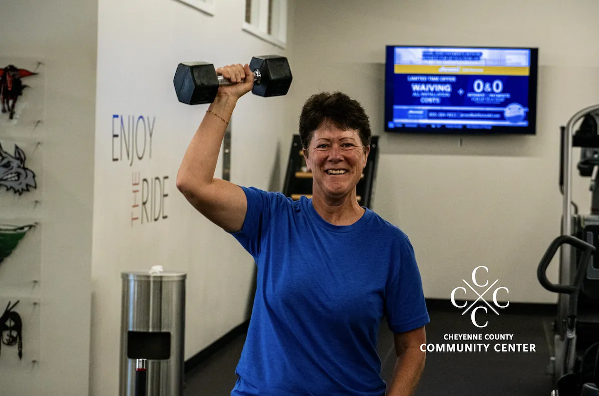 Smiling member in a blue shirt lifting a dumbbell at The Training Room