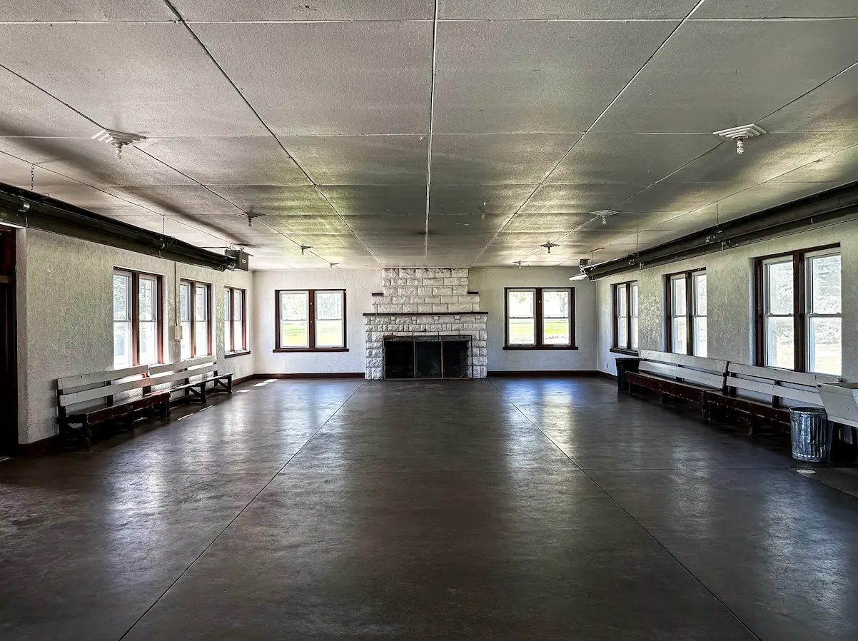 Open interior of the Legion Park Shelter House with stone fireplace and bench seating