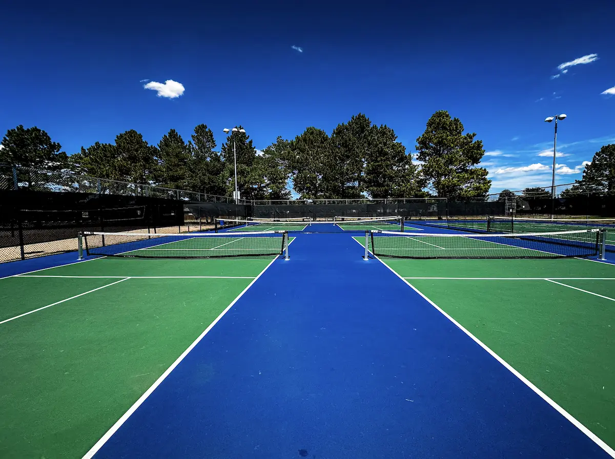 Outdoor pickleball courts with blue and green surfaces, nets and perimeter fencing at The Center
